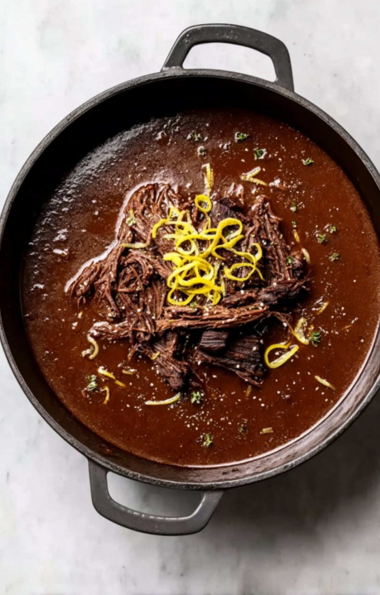 Slow-cooked, shredded beef cheeks in a concentrated dark reduction, garnished with bright yellow lemon zest strips.