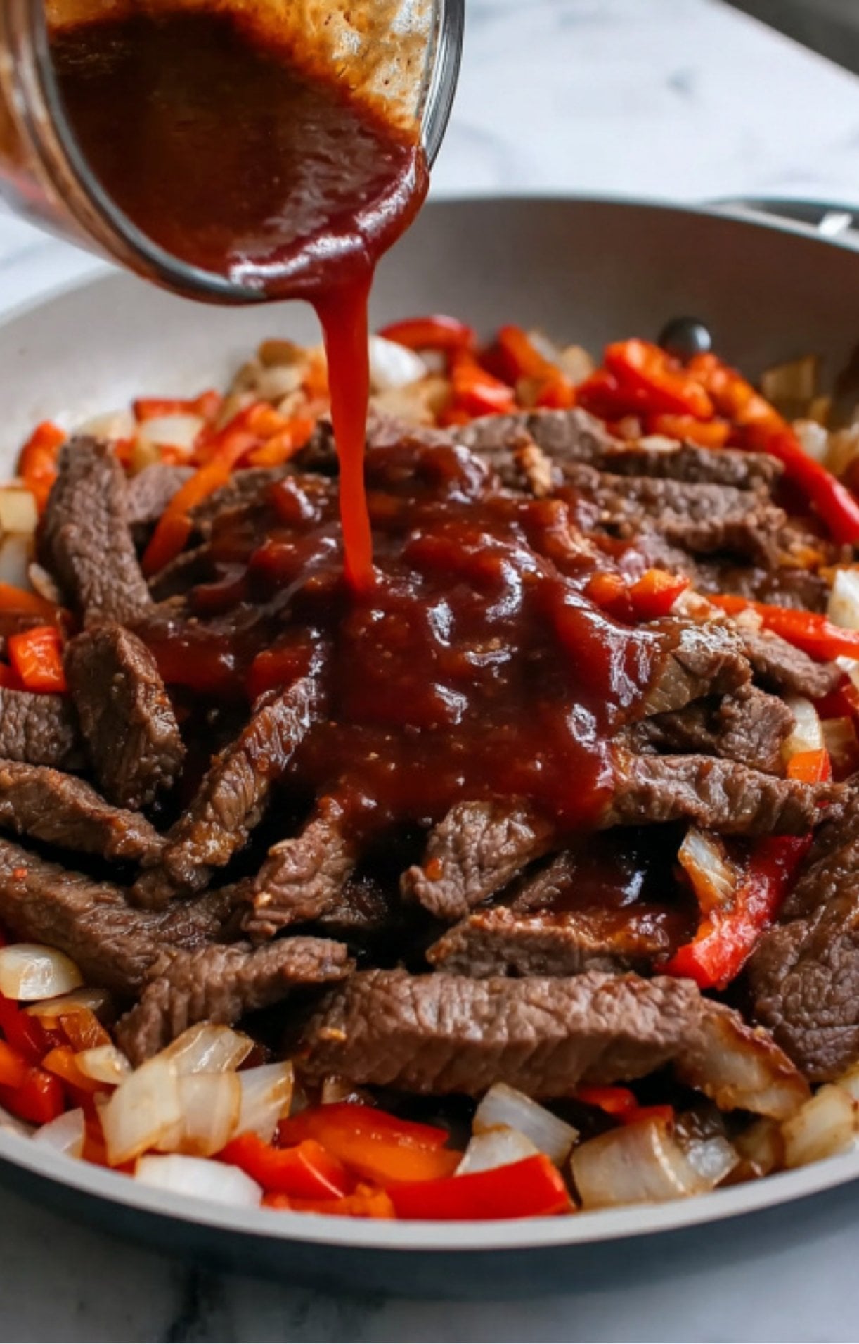 A thick, dark reddish-brown savory sauce being poured over the cooked beef and vegetables in a pan.