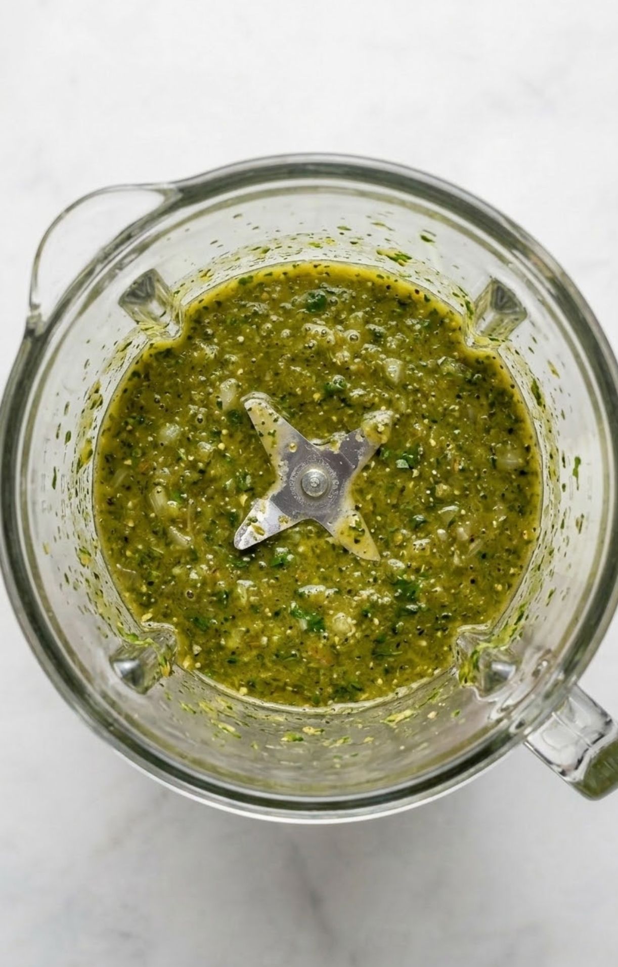 The inside of a blender containing a vibrant, thick green herb and spice marinade for the beer can chicken.