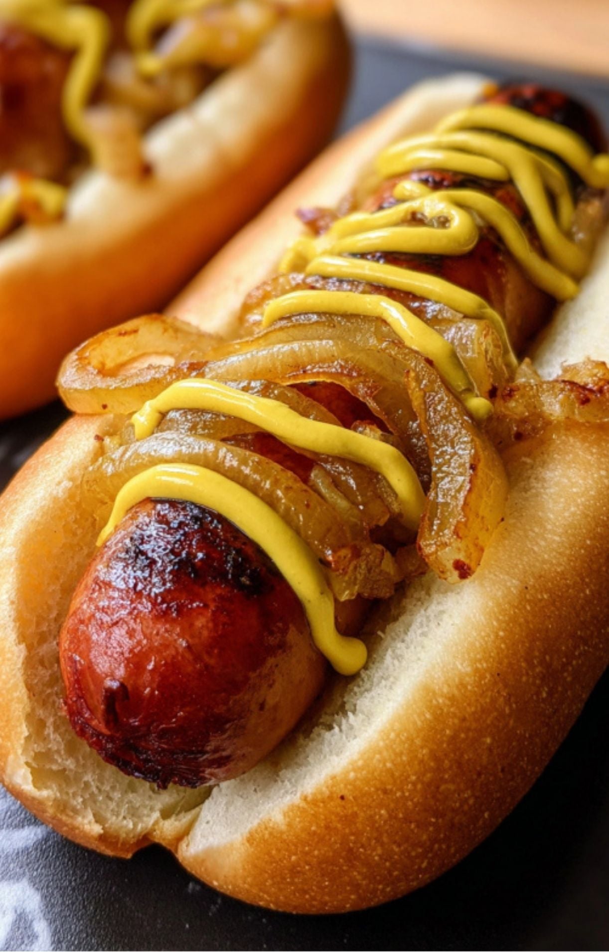 A macro shot of a single Smoked Beer Brat, highlighting the texture of the grilled sausage and glossy caramelized onions.