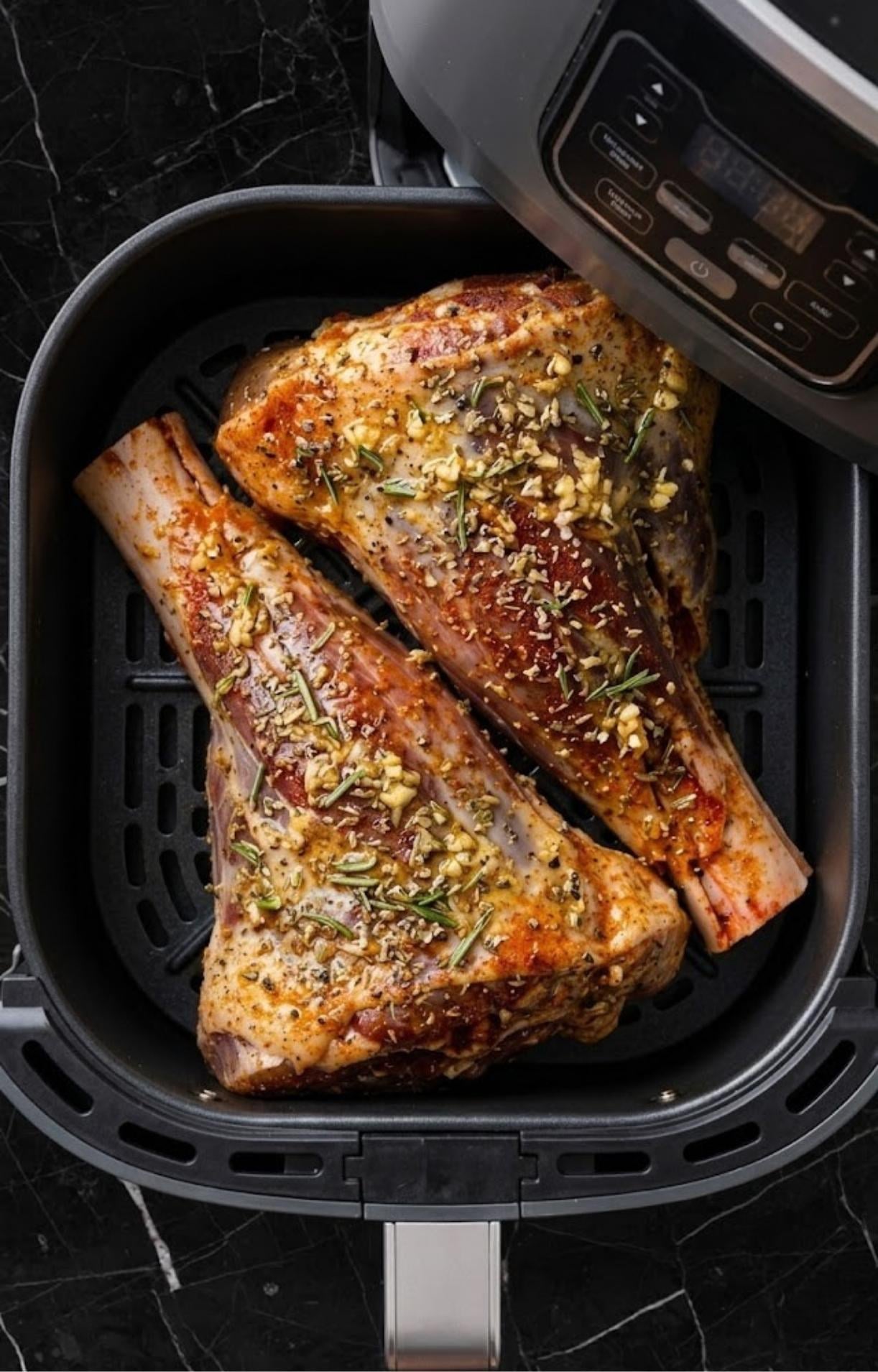 Seasoned lamb shanks placed inside a clean black air fryer basket before cooking.