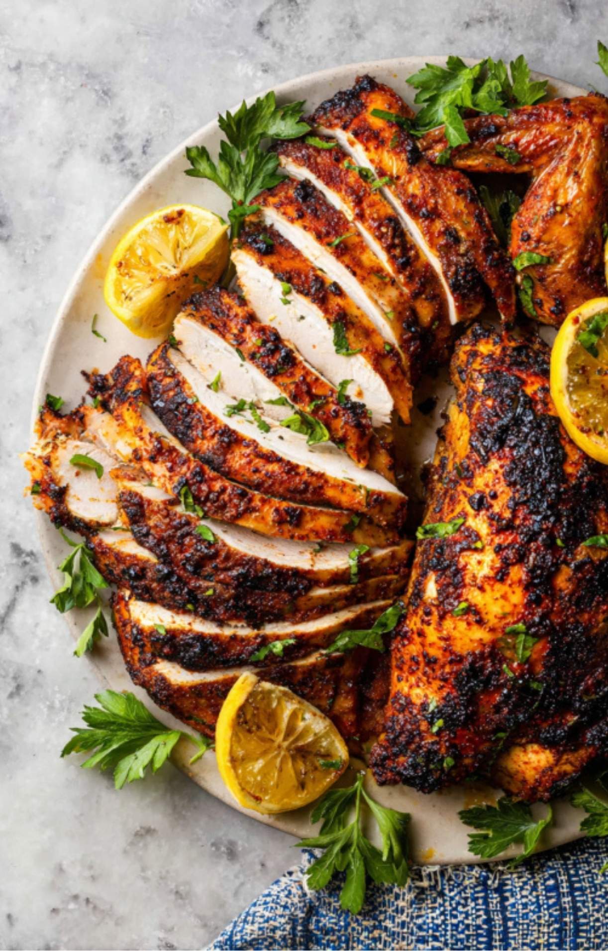 An overhead view of juicy, sliced chicken breast from a beer can chicken oven recipe, garnished with herbs and lemons.