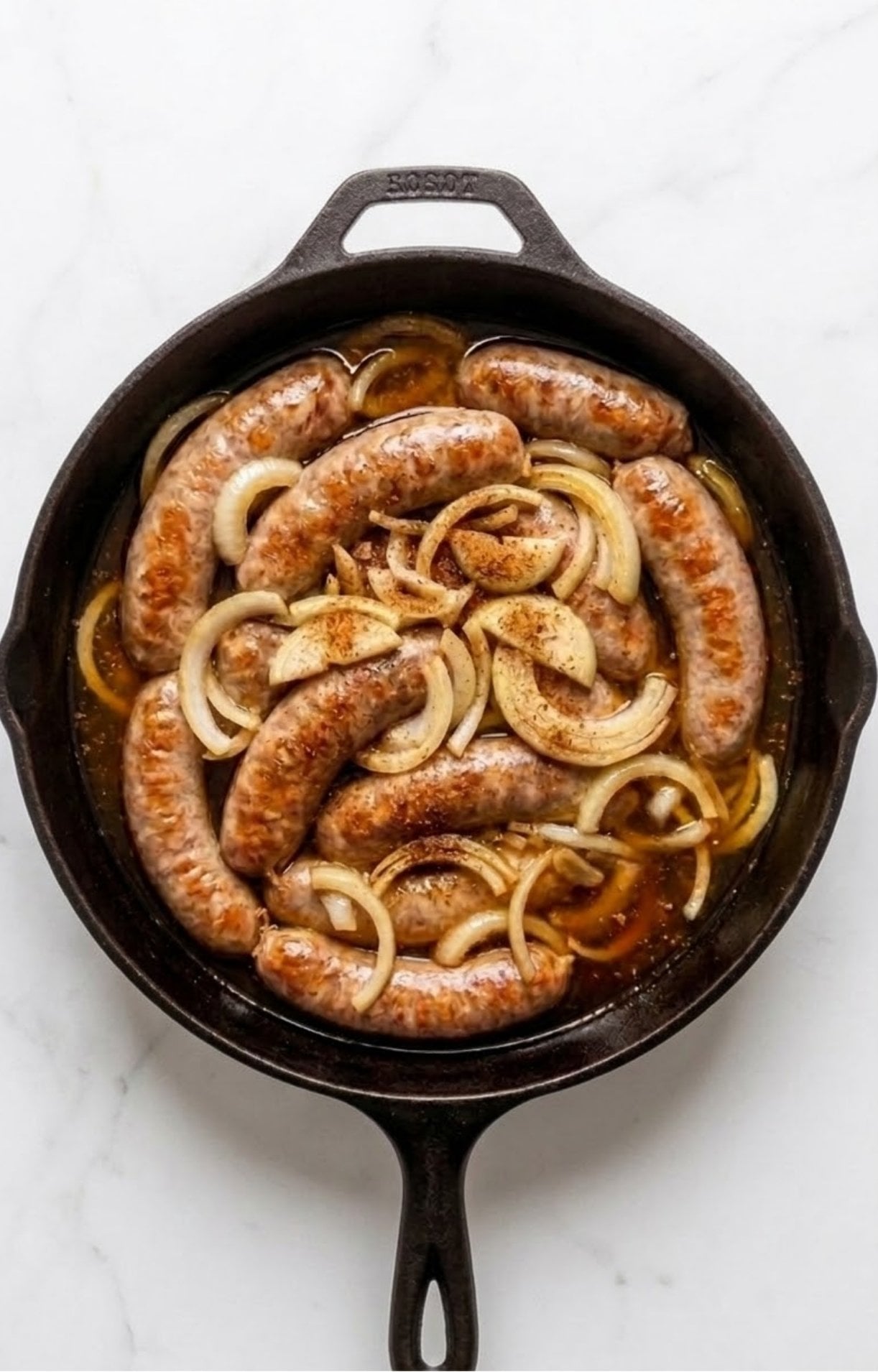 Bratwurst and onions simmering in a beer bath within a cast iron skillet, starting to turn opaque.