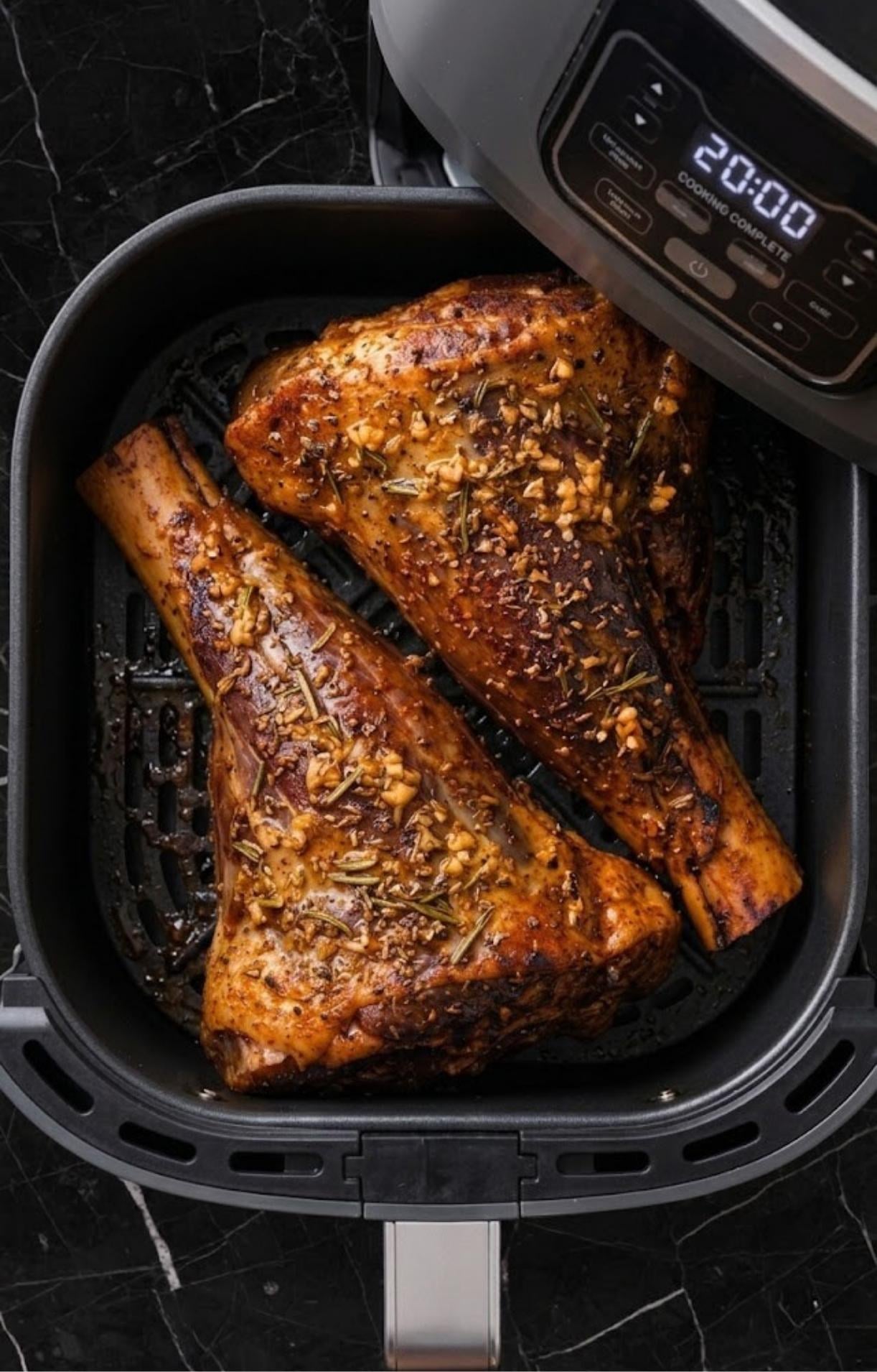 Lamb shanks in an air fryer basket showing a light golden-brown crust after the first stage of cooking.