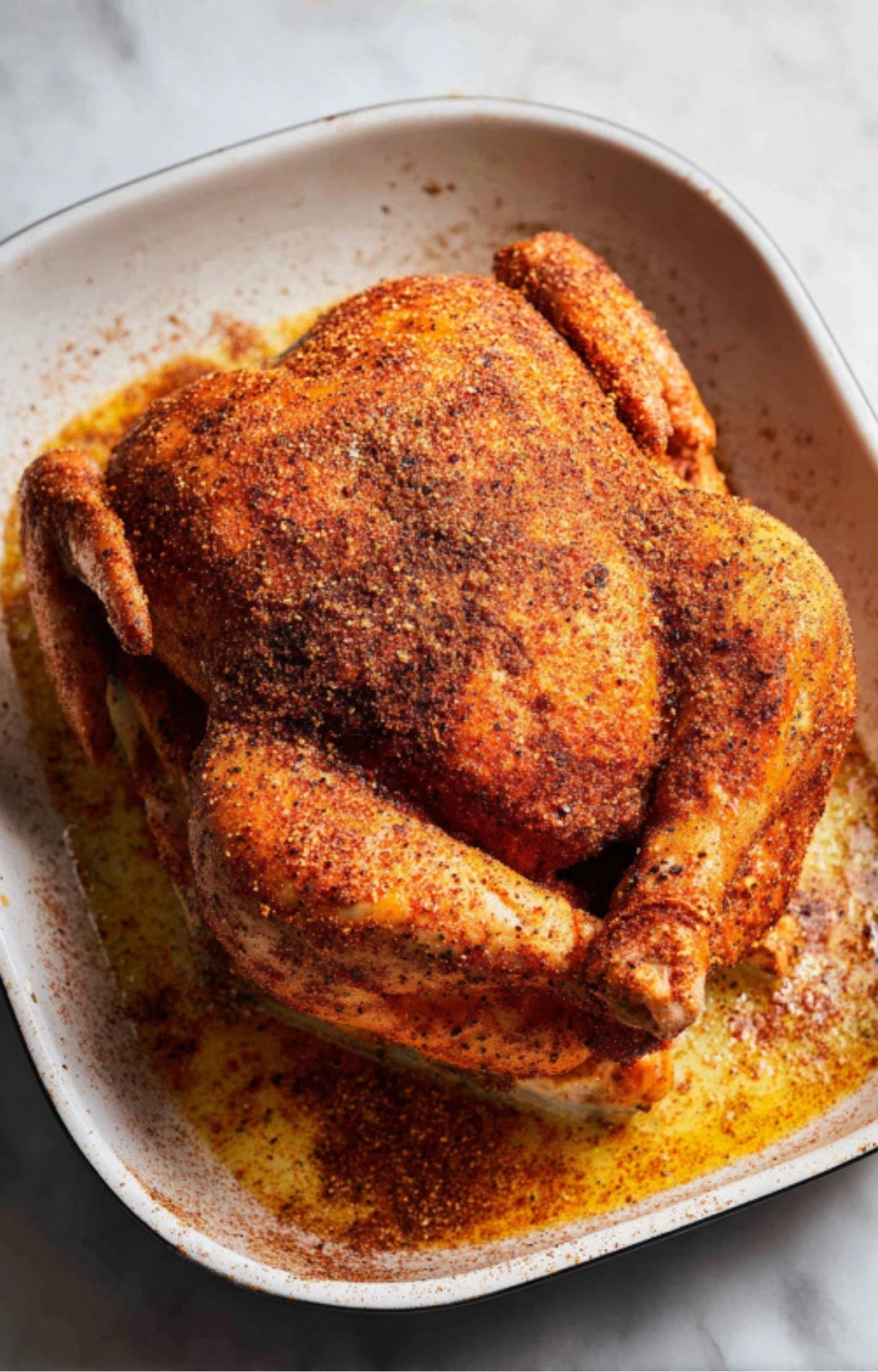 A raw whole chicken in a roasting dish generously coated in a red spice rub for a flavorful beer can chicken oven result.
