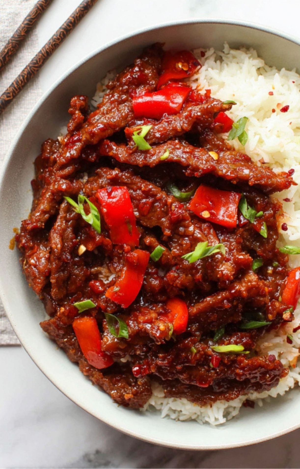 A serving of Beijing Beef with red peppers and green onions placed over a bed of fluffy white steamed rice.