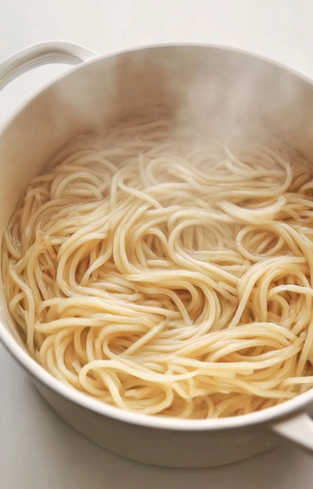 Fresh lo mein noodles simmering in a pot of boiling water with steam rising from the surface.