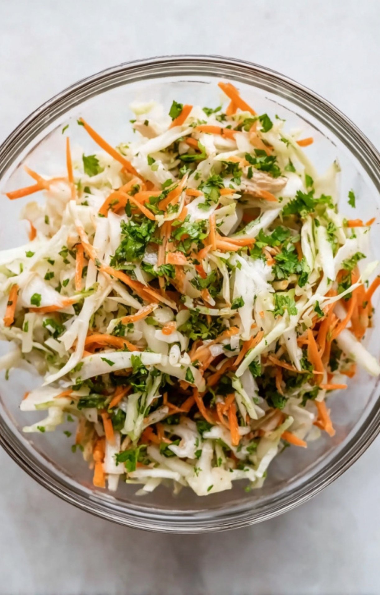 A glass bowl filled with a crisp slaw made of shredded cabbage, carrots, and fresh cilantro to top the Beer Can Chicken Tacos.