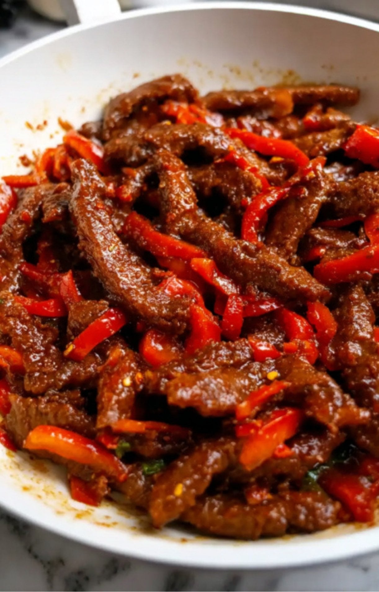 The beef and red peppers simmering together in the pan as the sauce thickens and coats every piece.