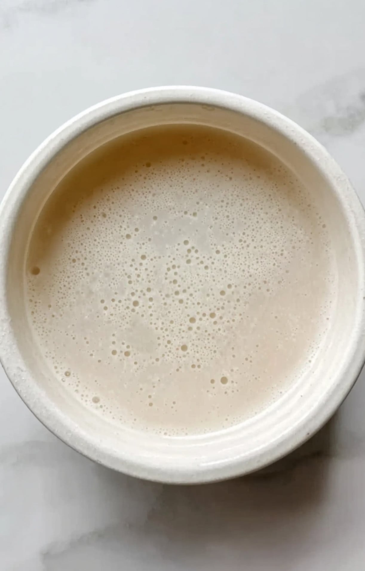 A small white bowl containing a smooth, opaque white cornstarch and water mixture used for thickening the stir-fry.