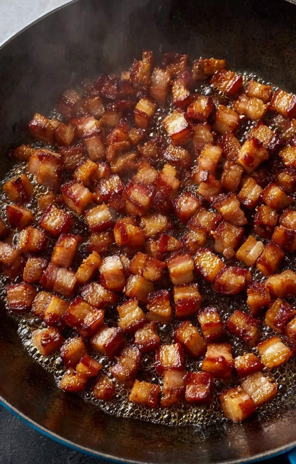 Close-up of dilled pancetta or bacon lardons browning in a cast iron skillet until golden and crispy for a savory ragu base.
