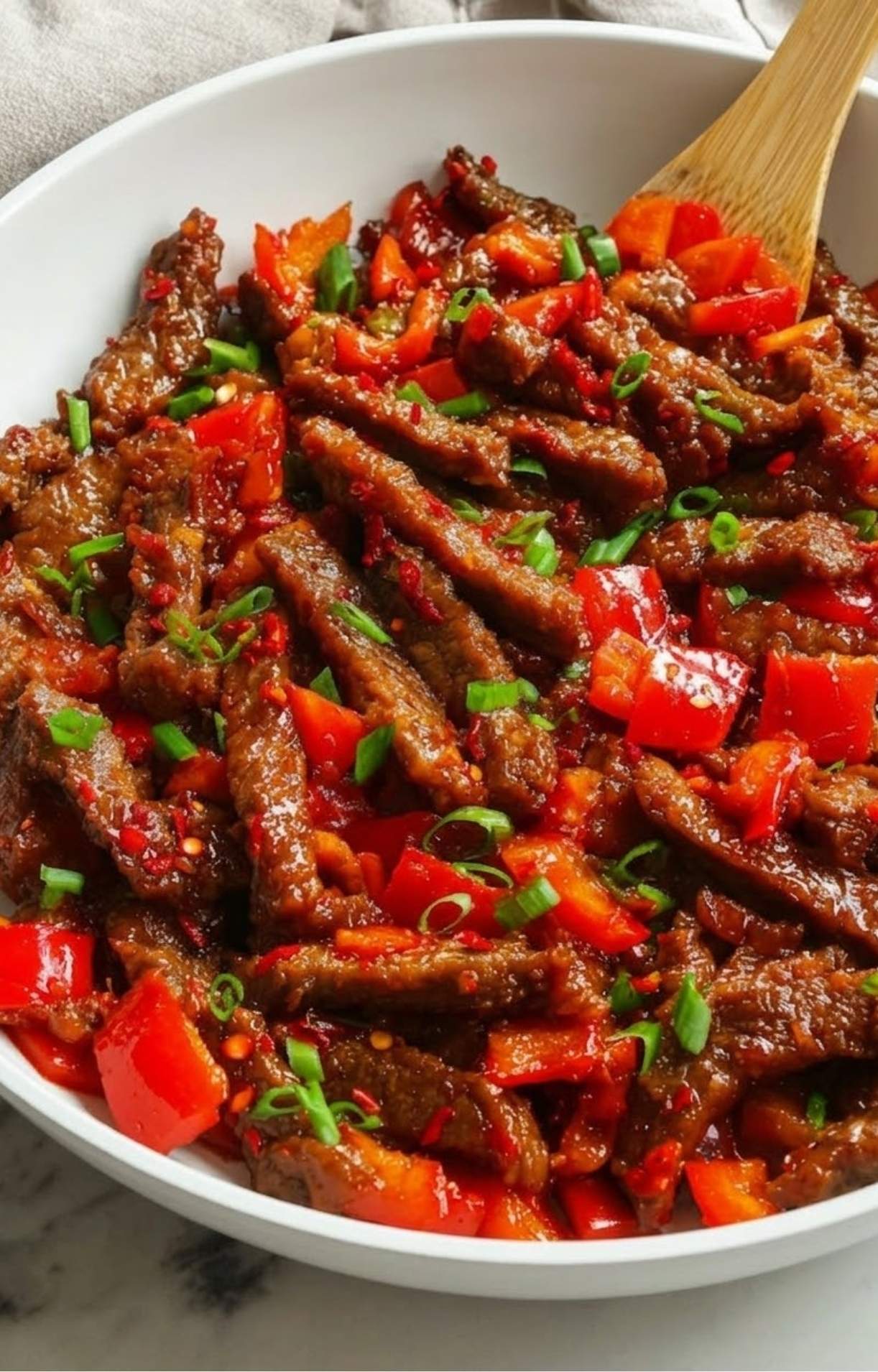 A white bowl filled with crispy Beijing Beef strips, vibrant red bell peppers, and a garnish of fresh green onions.