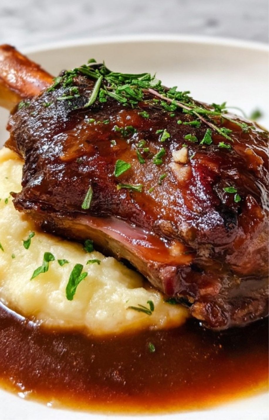 A plated lamb shank served on a bed of creamy mashed potatoes with fresh herb garnish.