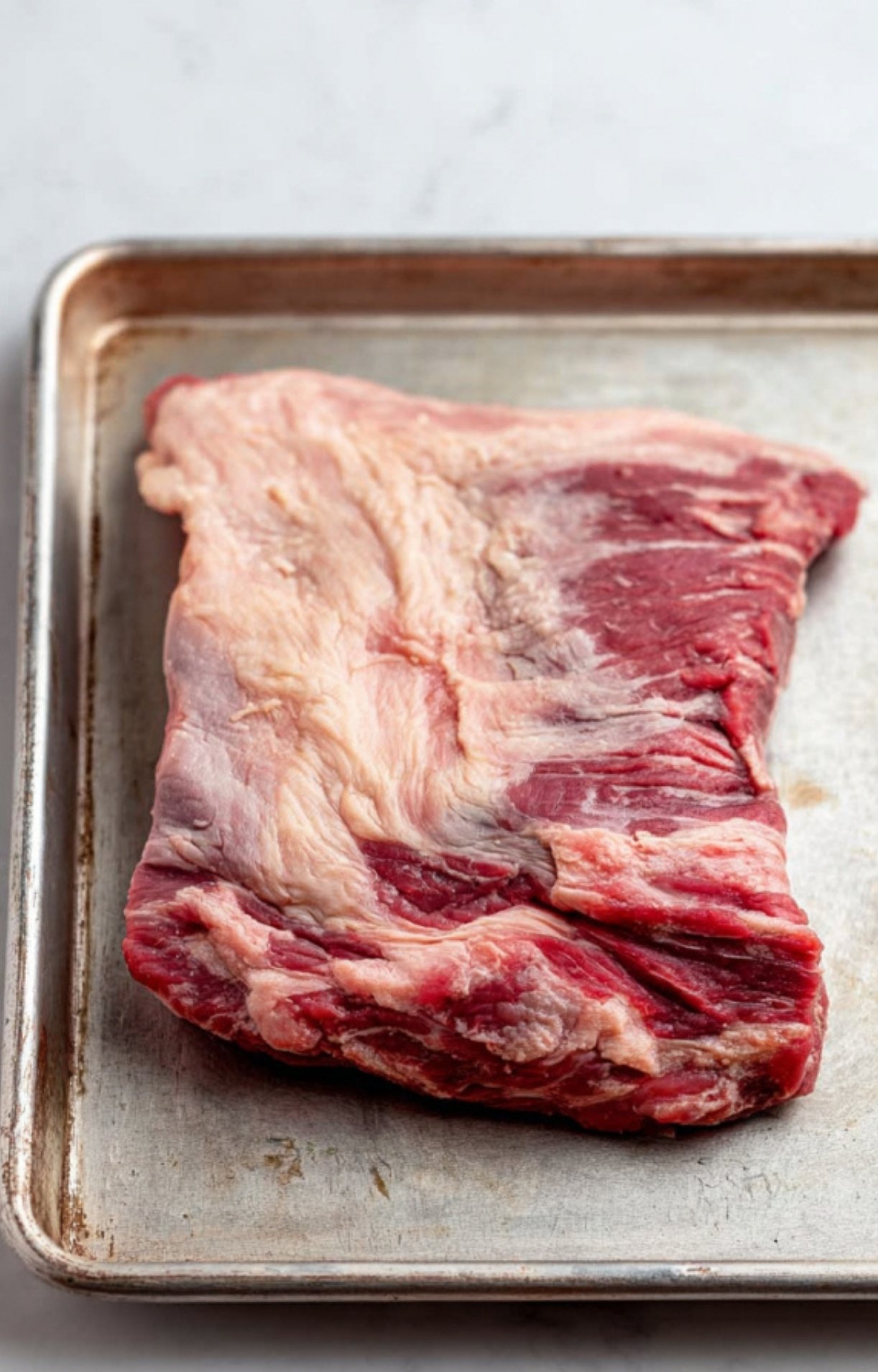 A raw slab of beef brisket on a metal baking sheet ready to be trimmed for Smoked Beef Brisket Burnt Ends.