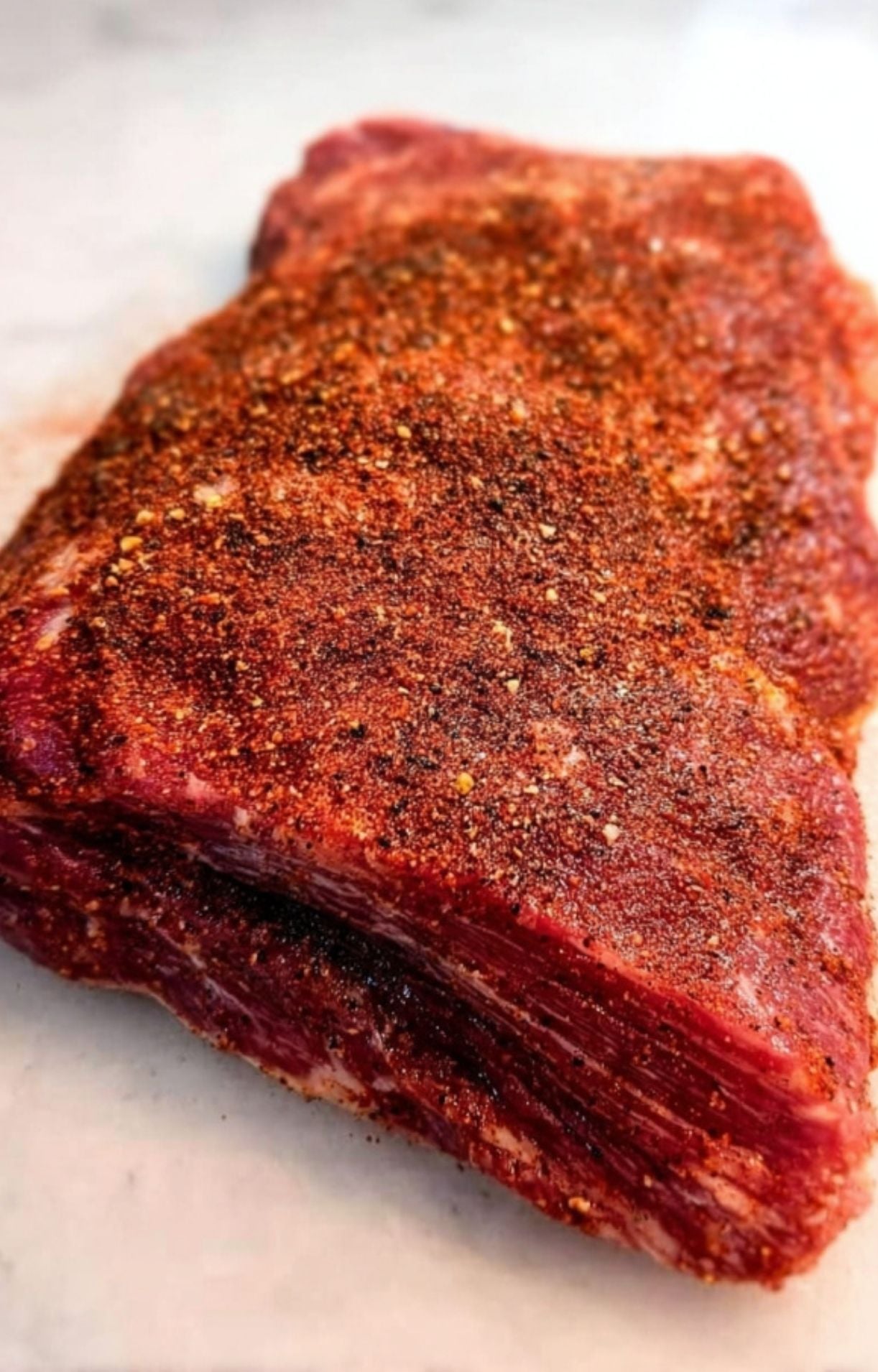 Raw beef brisket generously coated in a red spice rub consisting of paprika, garlic, and pepper.