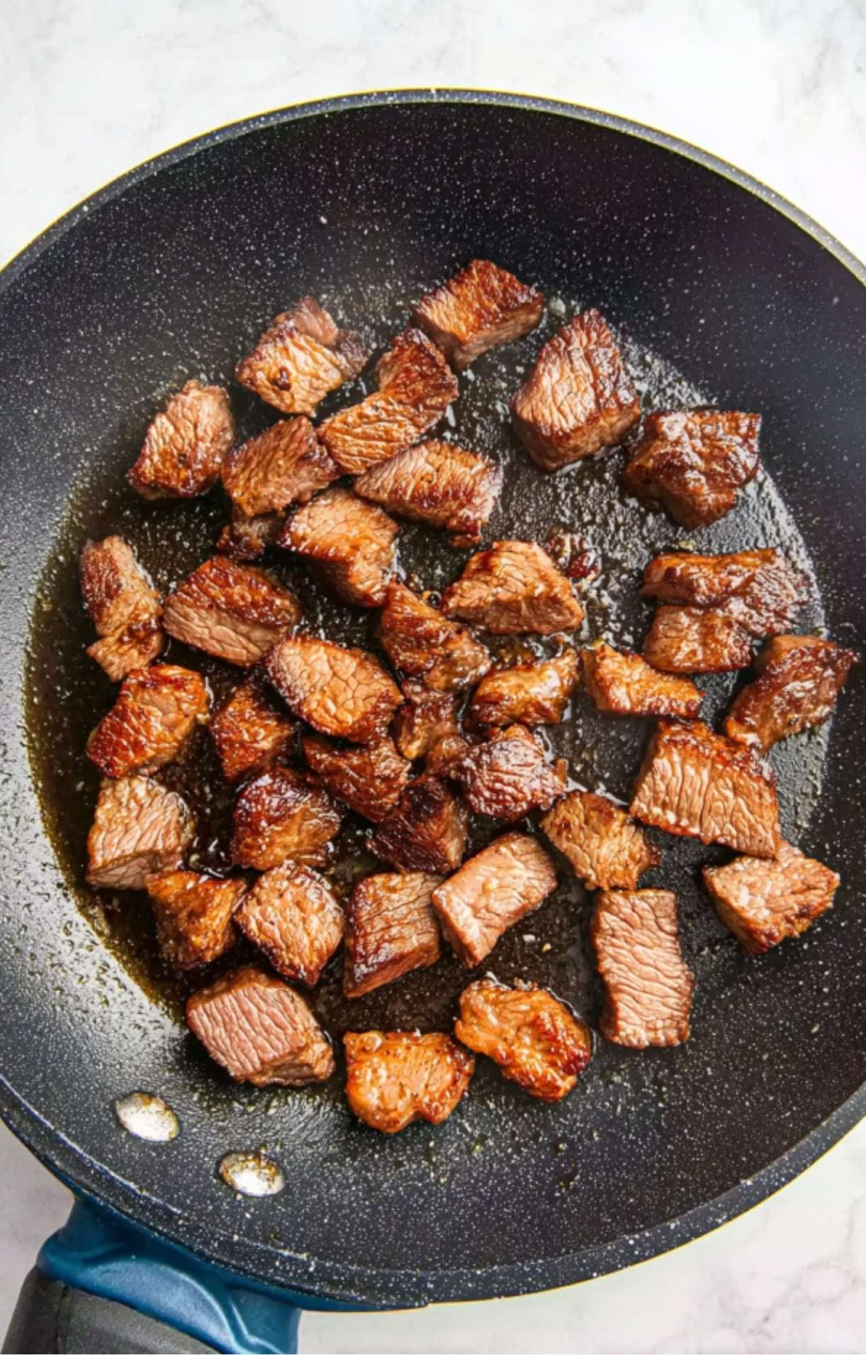 Sliced pieces of brisket being browned in a dark non-stick skillet with oil to build flavor for Smoked Brisket Chili.