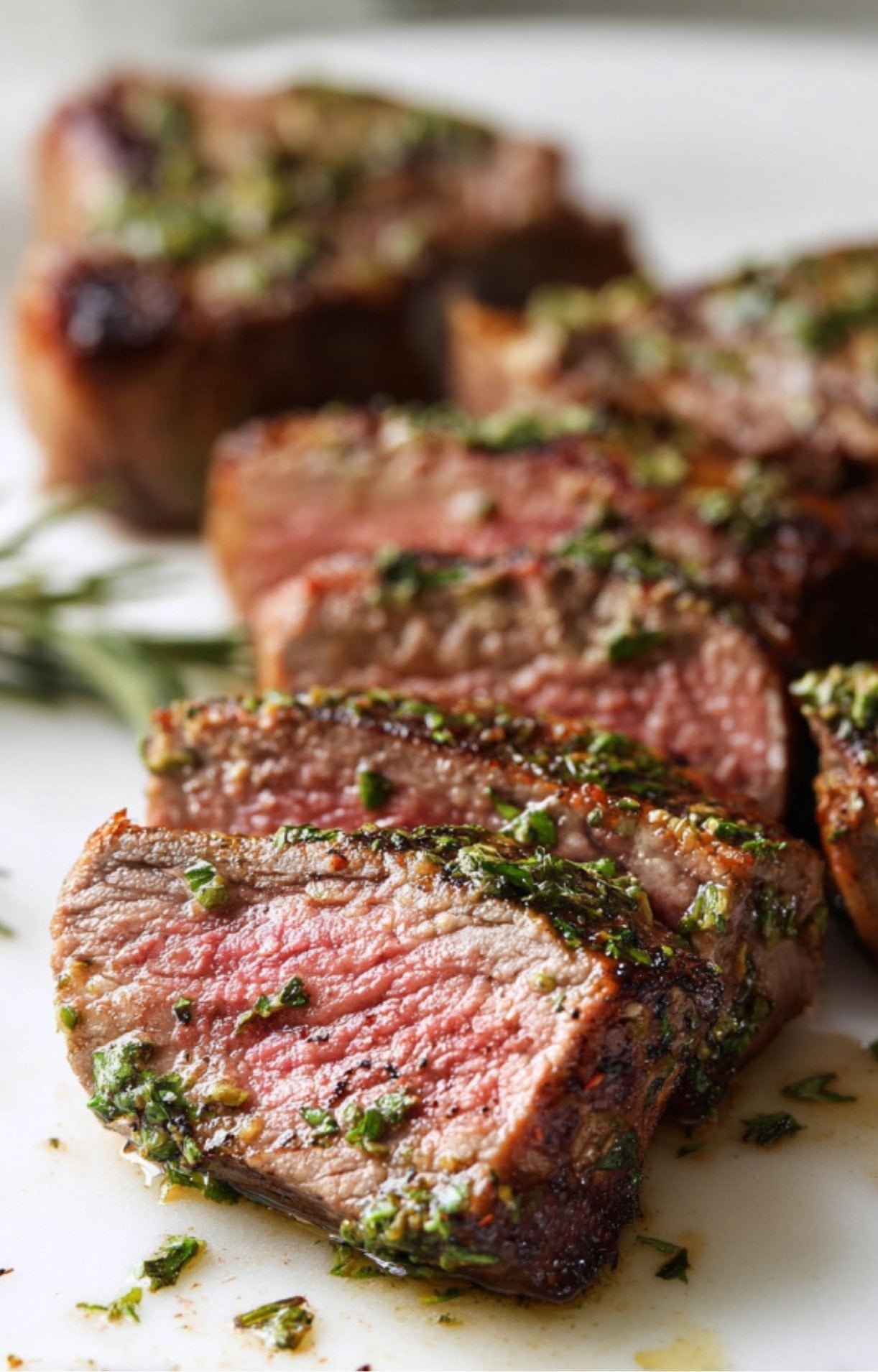 Close-up of sliced air fryer lamb chops showing a perfectly cooked pink interior and a crust of minced garlic and green herbs.