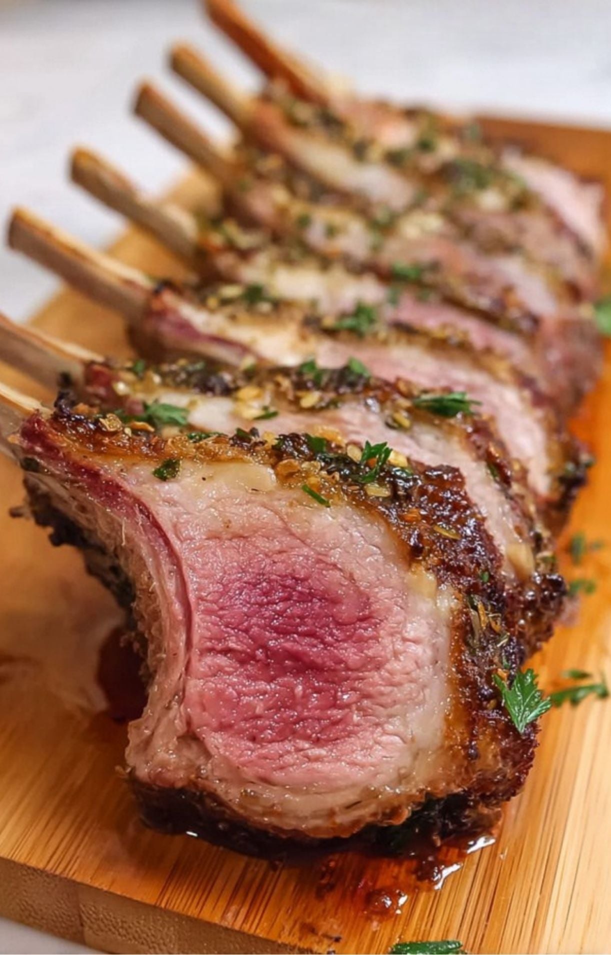 A row of perfectly sliced lamb chops resting on a wooden cutting board, showcasing the tender meat and crispy herb topping.