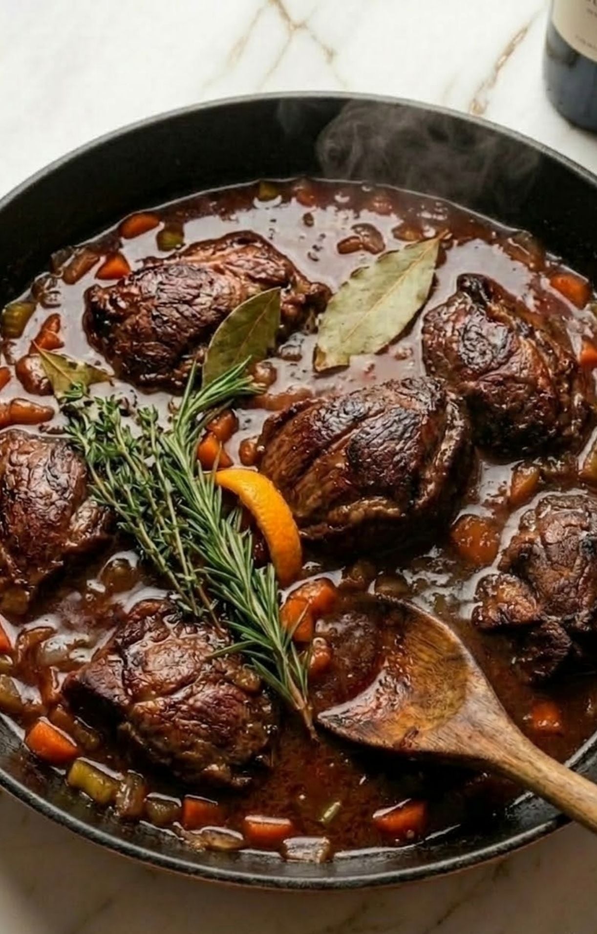 The seared beef cheeks simmering in a rich red wine sauce with fresh rosemary, bay leaves, orange peel, and diced vegetables.