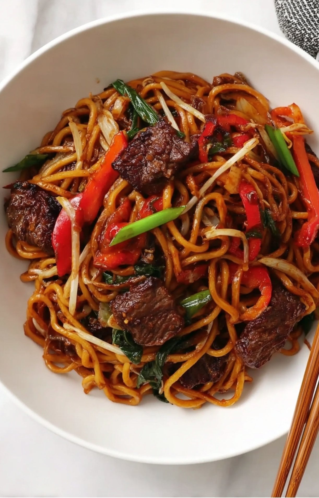 A large white bowl filled with Beijing Beef Noodles, showing the glossy noodles tossed with tender beef and crisp vegetables.