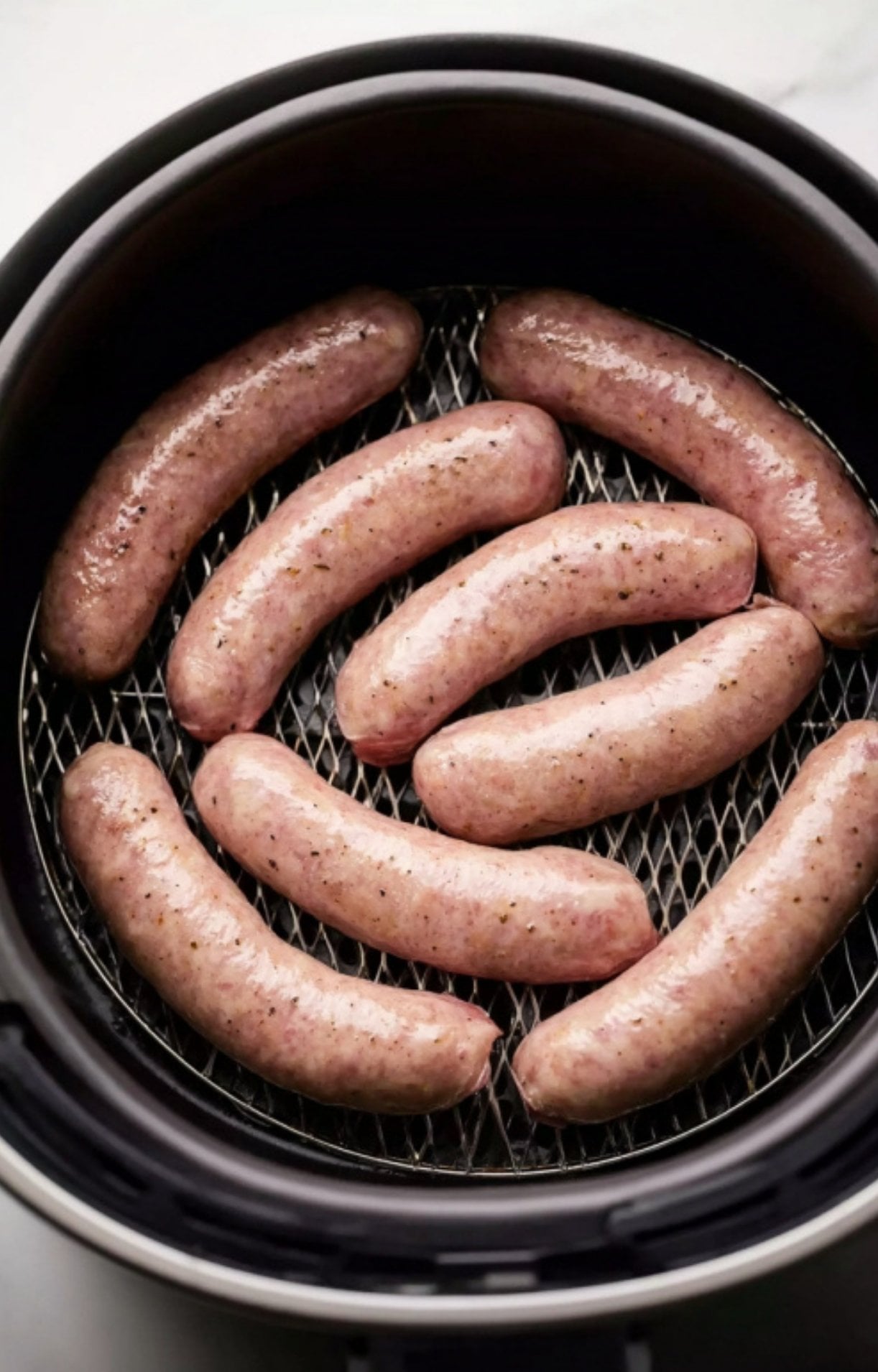 Raw beer brats arranged in a single layer in a black air fryer basket before cooking.
