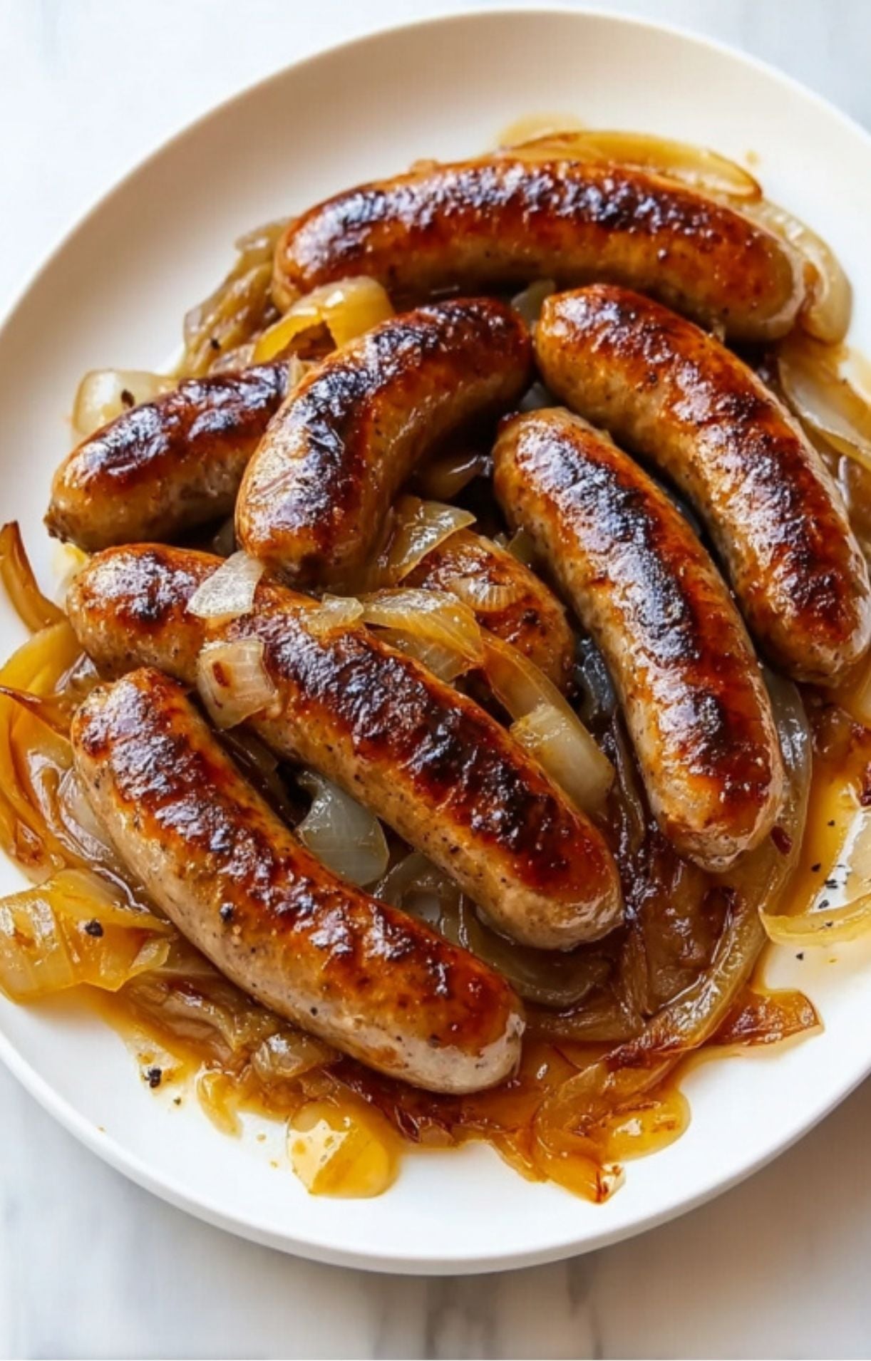 Seven perfectly seared bratwurst sausages nestled in a mound of tender, translucent onions on a round serving plate.