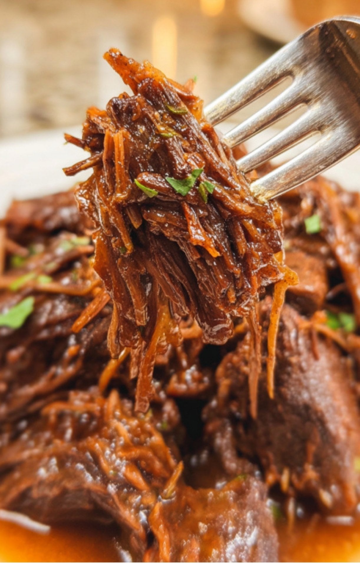 A close-up of shredded braised beef cheeks on a fork, showing the succulent, fall-apart texture.