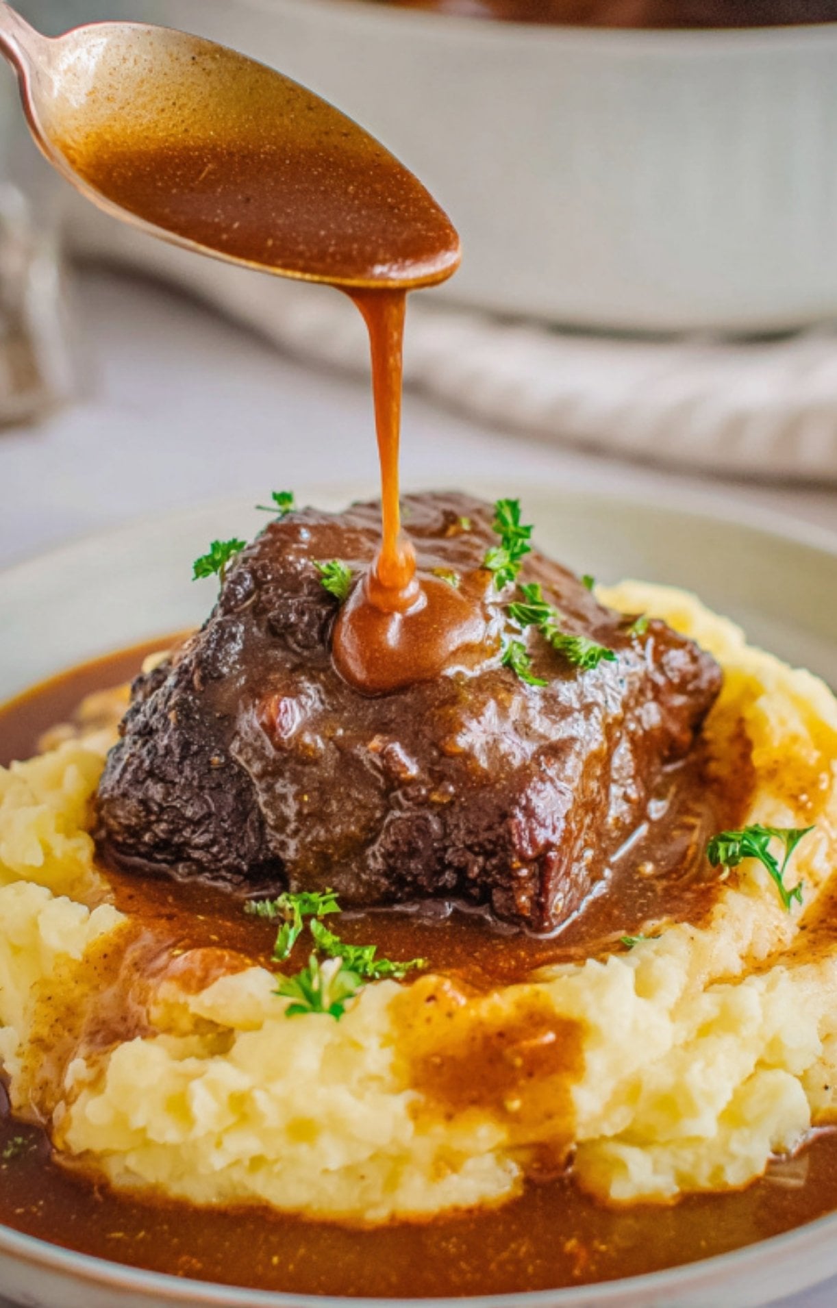 Rich brown gravy being poured over a tender braised beef cheek resting on a bed of creamy mashed potatoes.
