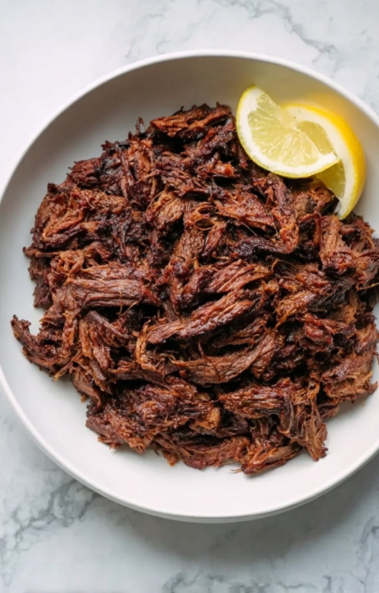 A white bowl filled with juicy, shredded beef cheek meat garnished with a fresh lemon wedge.