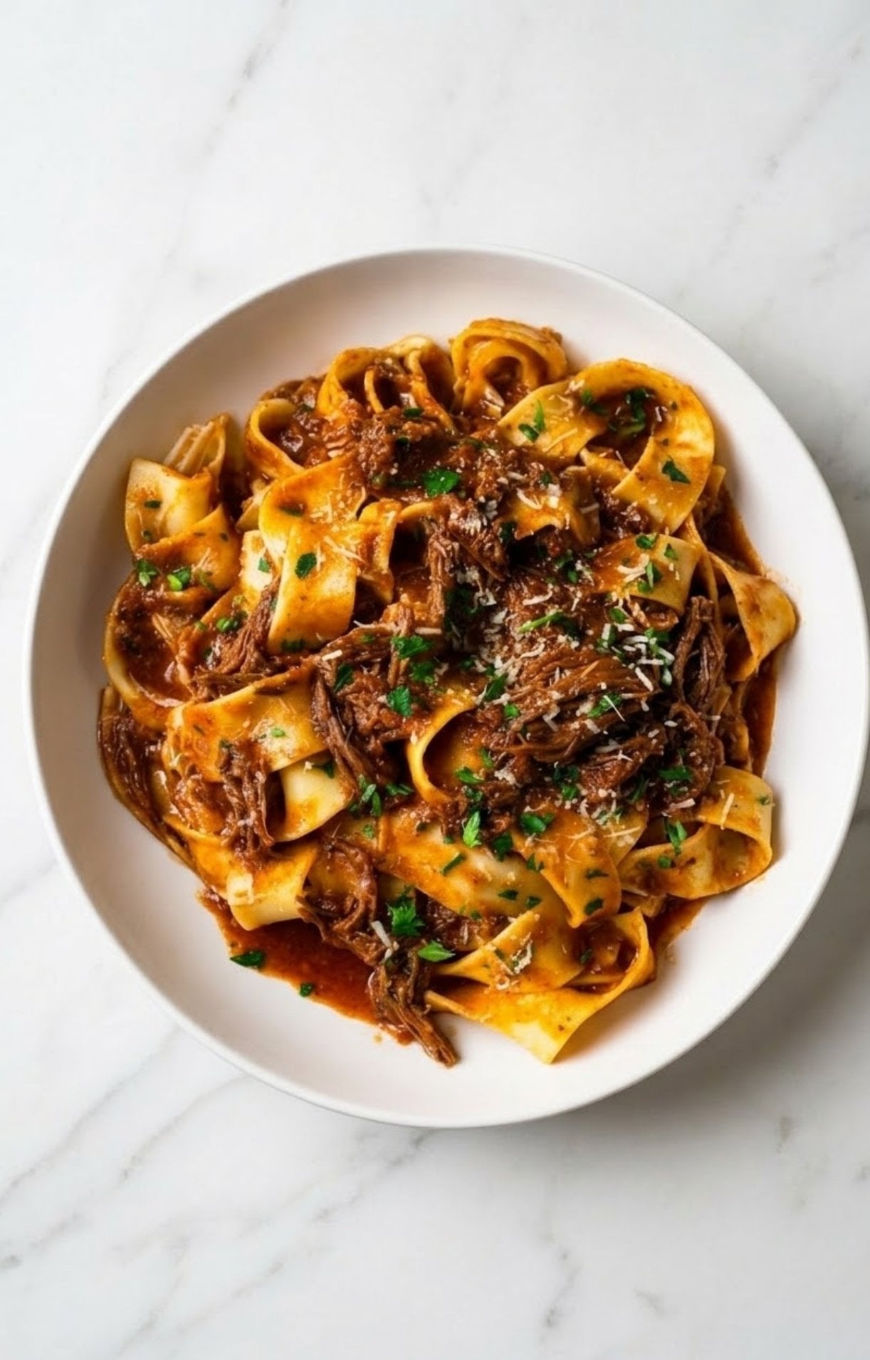 A top-down view of a white bowl filled with Beef Cheek Ragu and pappardelle, garnished with fresh parsley and grated cheese.