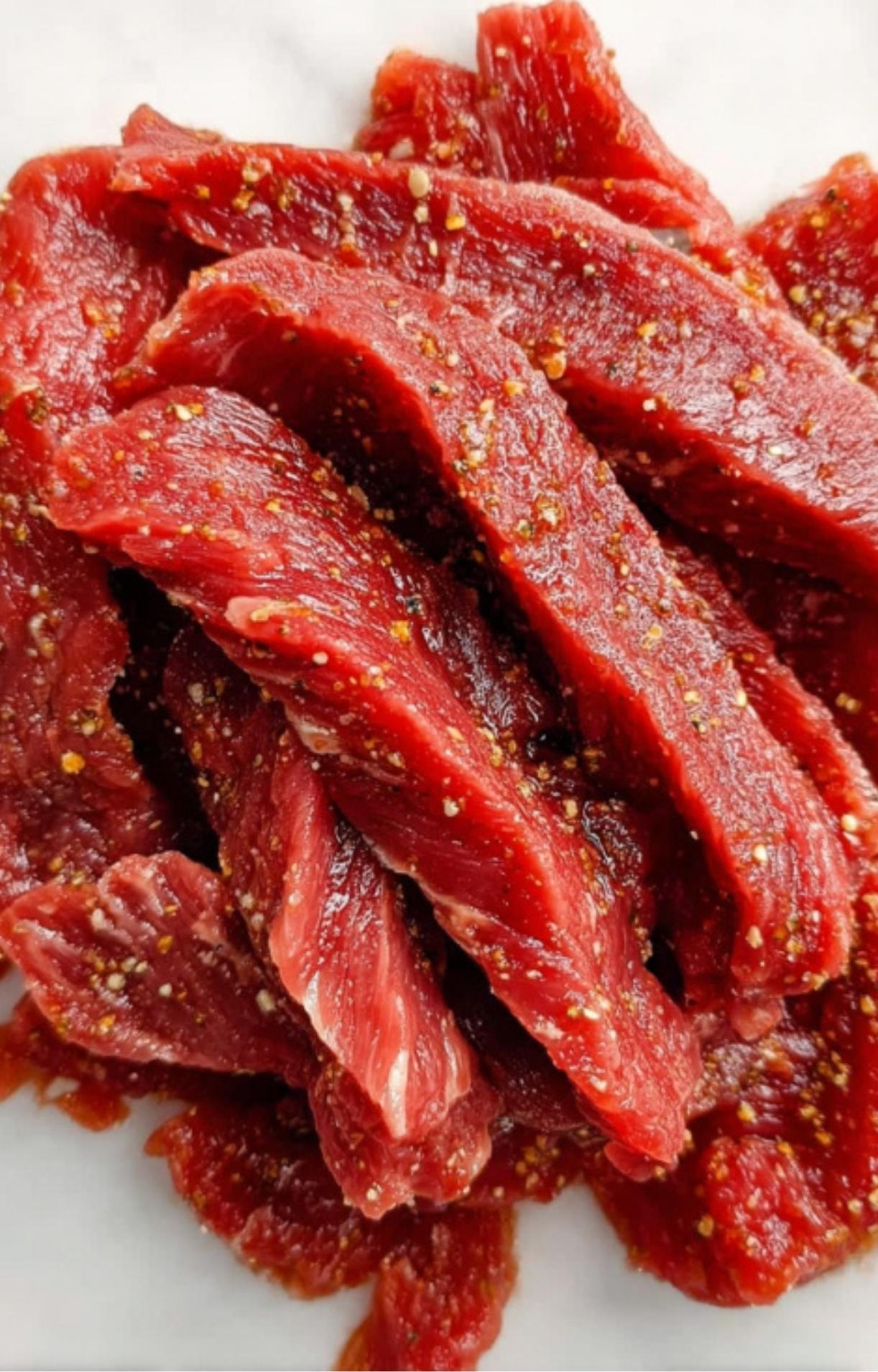 Thinly sliced strips of raw red beef seasoned thoroughly with salt, pepper, and spices before the coating process.