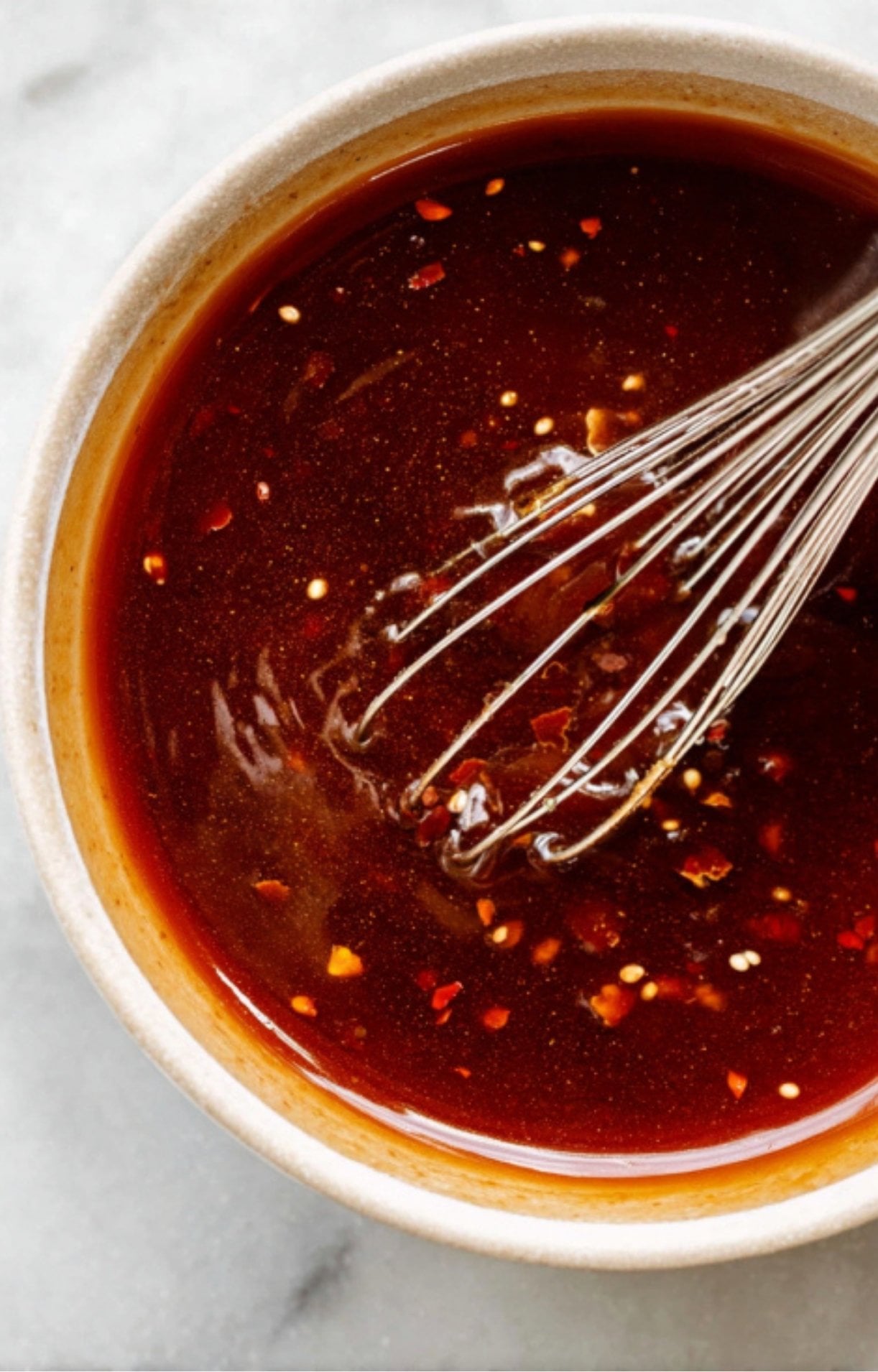 A small bowl containing a dark, savory-sweet stir-fry sauce being whisked with red chili flakes for a spicy kick.