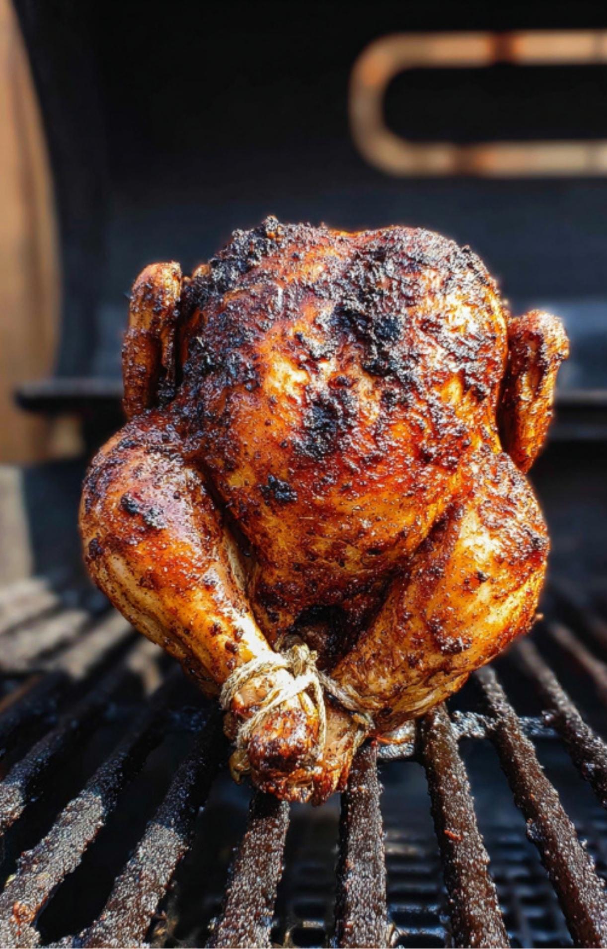 A fully cooked, dark golden-brown chicken standing on a beer can inside a smoker or grill, showing a crispy exterior.