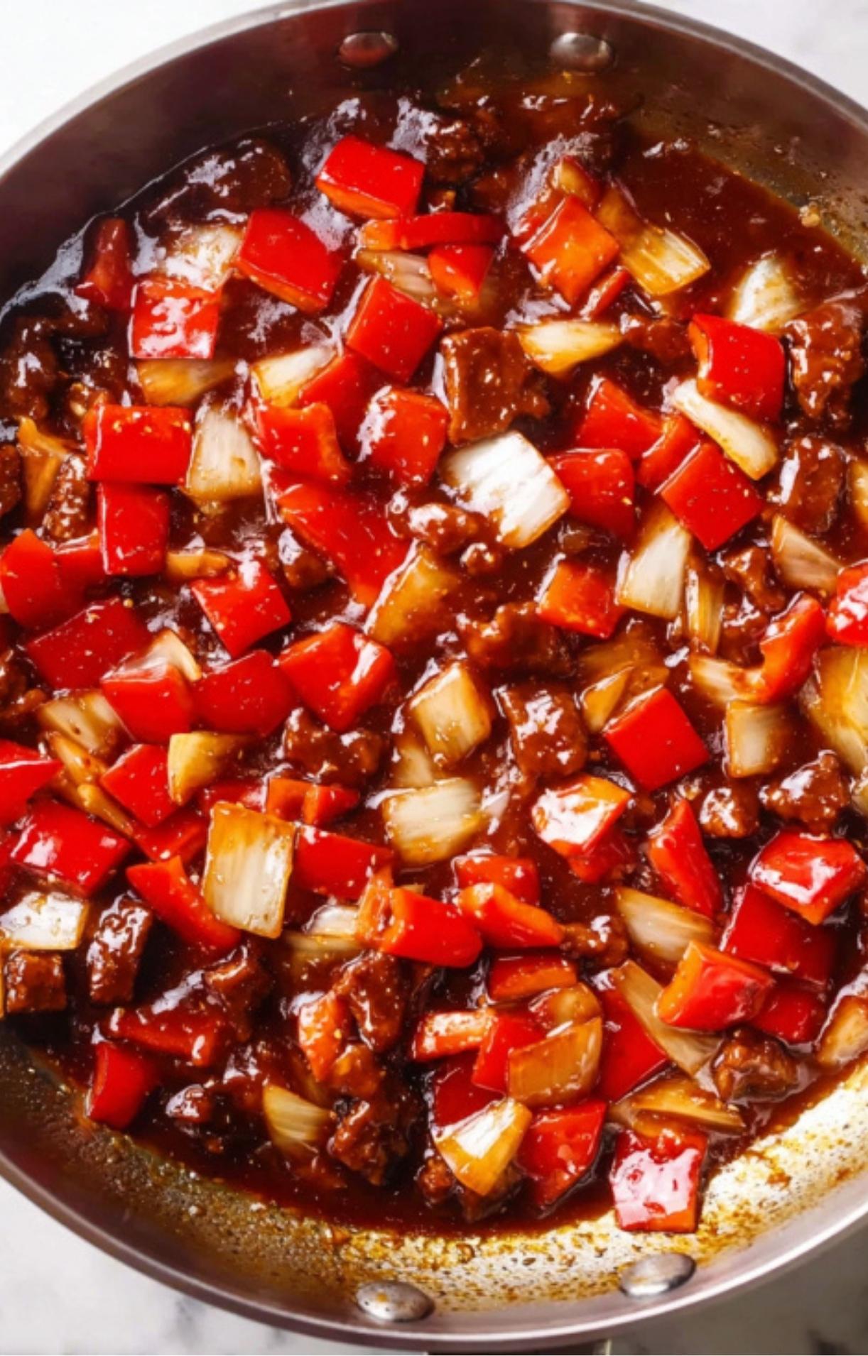 The sautéed peppers and onions simmering in a thick, dark Beijing sauce in a stainless steel pan.