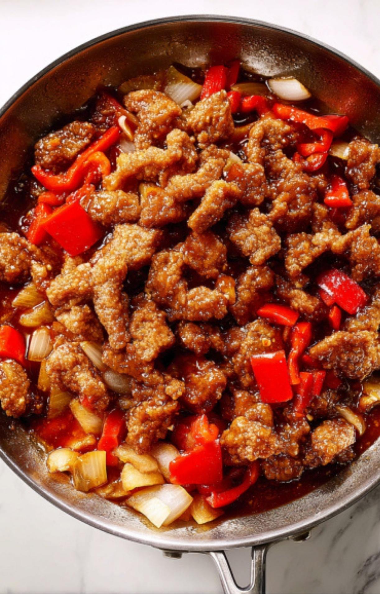 The final cooking stage where the fried beef strips are tossed back into the pan with the sauce and vegetables to coat everything evenly.