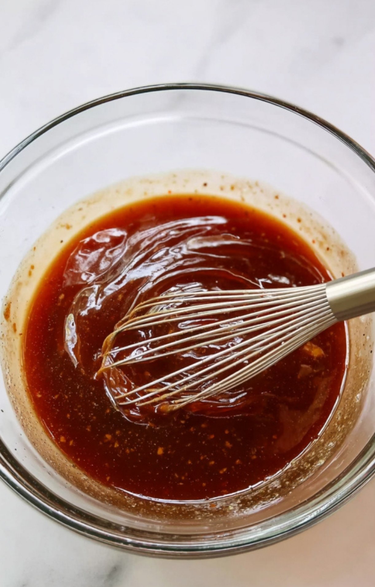 A metal whisk stirring together the dark, savory soy-based sauce for a Beijing beef and broccoli recipe.