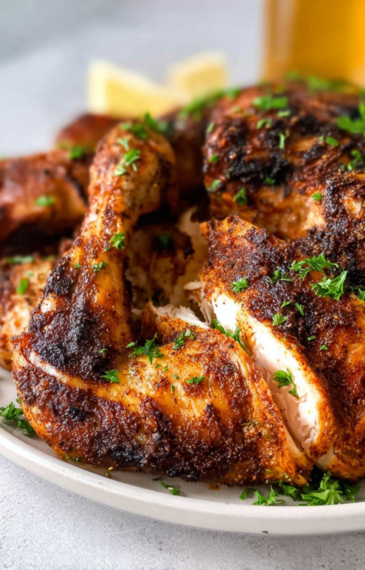 A close-up shot of juicy, sliced beer can chicken garnished with fresh parsley on a white plate, showing the beautifully charred, seasoned skin.