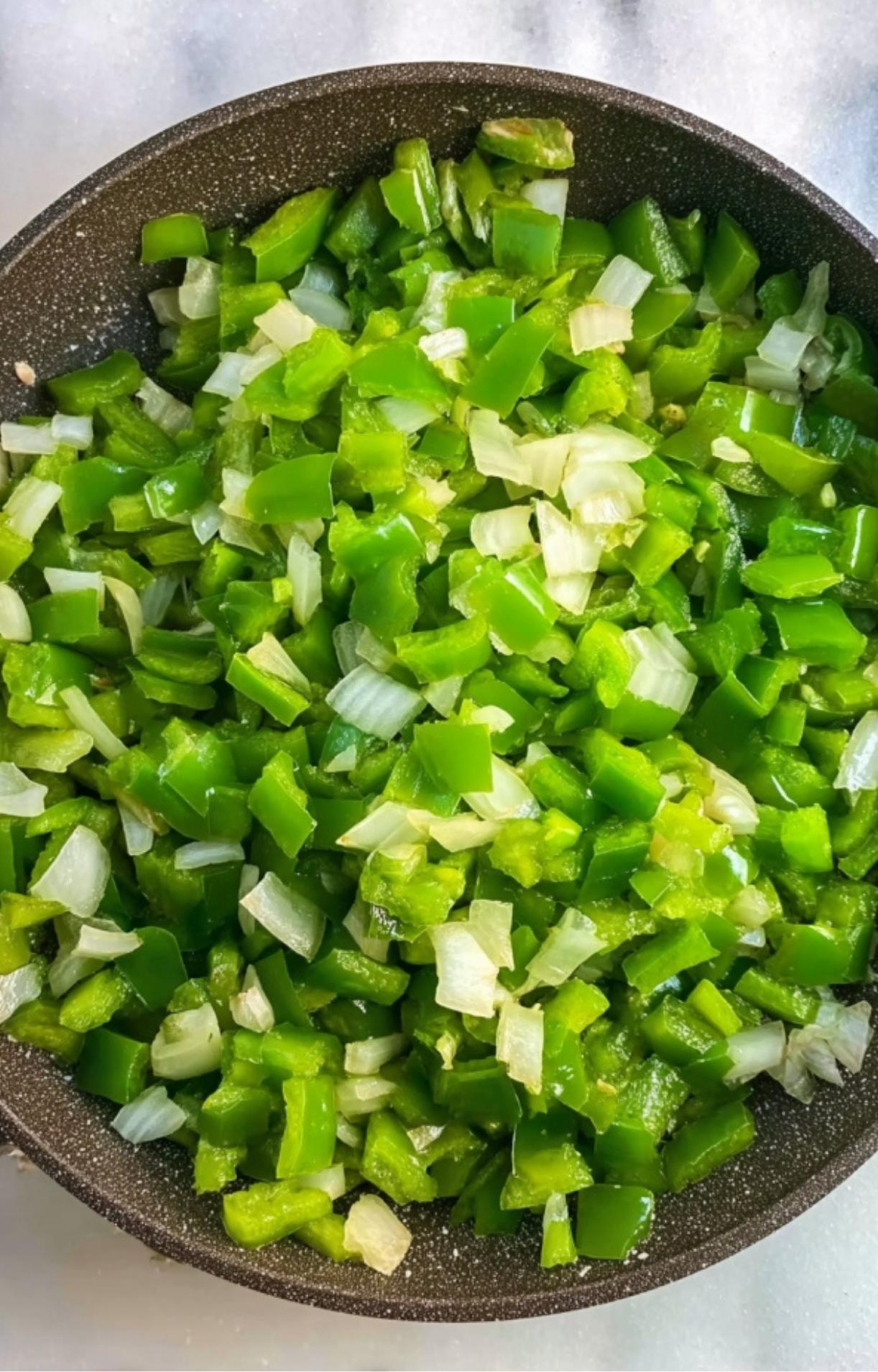 A pan filled with finely diced green bell peppers and white onions being softened as a base for Smoked Brisket Chili.
