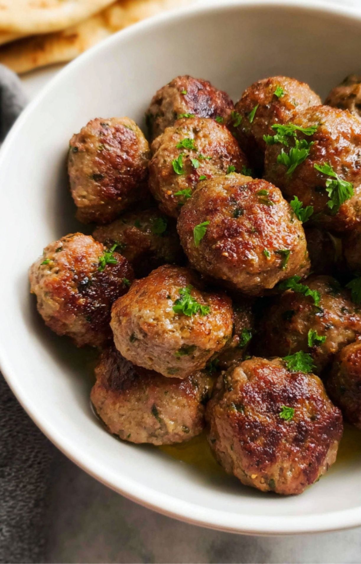 A white bowl of succulent, browned meatballs topped with a sprinkle of bright green parsley.