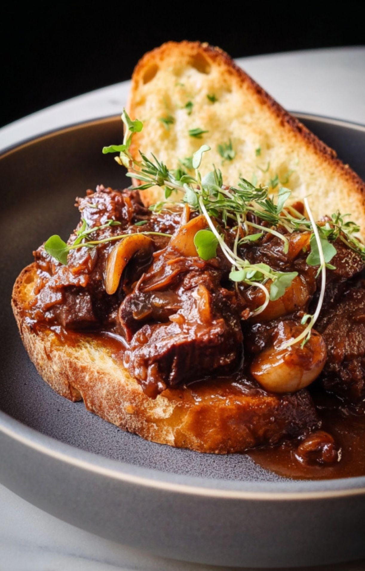 Detailed shot of succulent braised beef cheeks and rich gravy piled onto crusty bread with fresh thyme garnish.