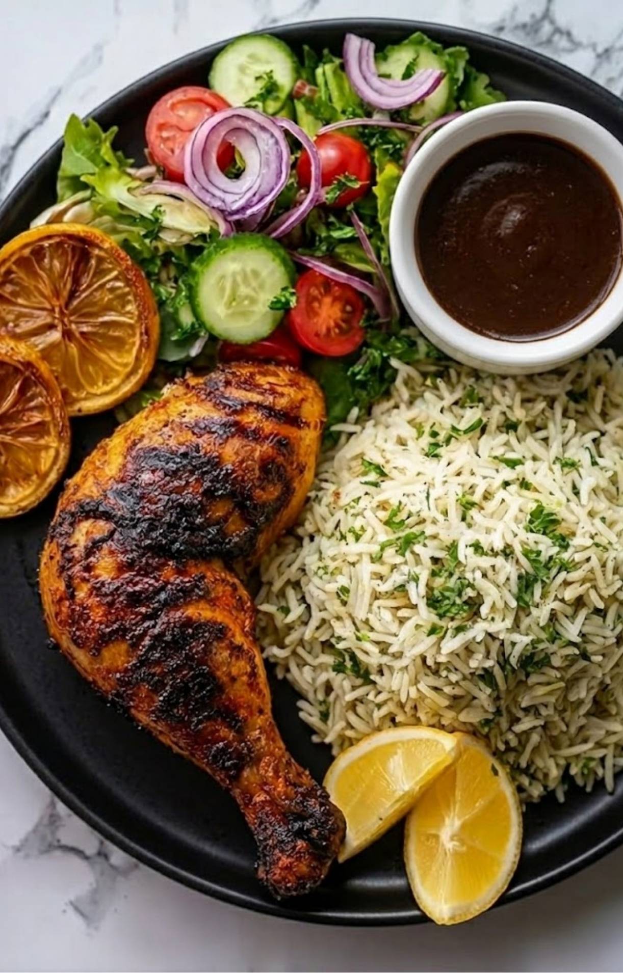 A single serving on a black plate featuring a grilled chicken leg, a heap of herb-flecked rice, a fresh garden salad, and dipping sauce.
