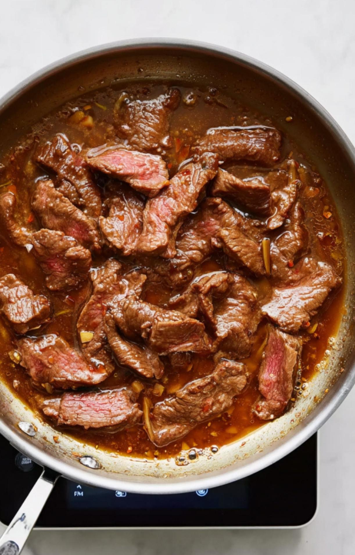 Marinated beef strips browning in a skillet to lock in flavor for a Beijing beef and broccoli dish.