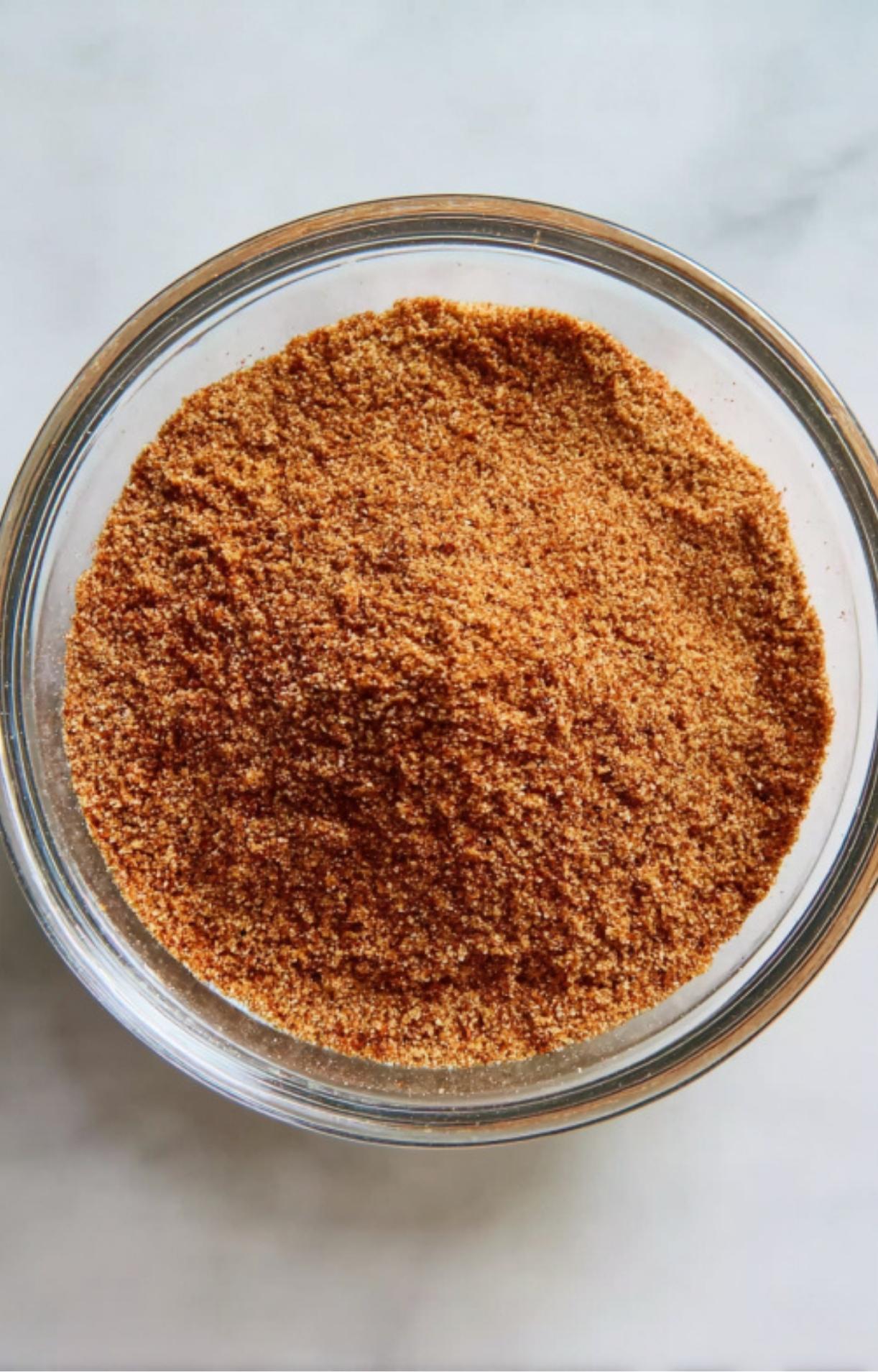 A glass bowl filled with a fine, reddish-brown spice rub consisting of sugar, paprika, and garlic powder for seasoning poultry.