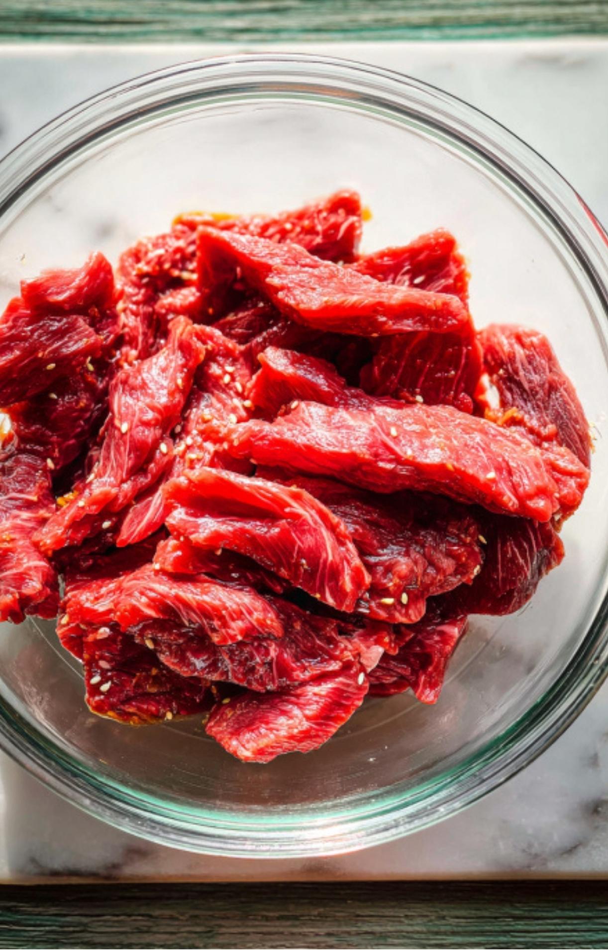 Thinly sliced raw flank steak in a clear glass bowl ready for seasoning.