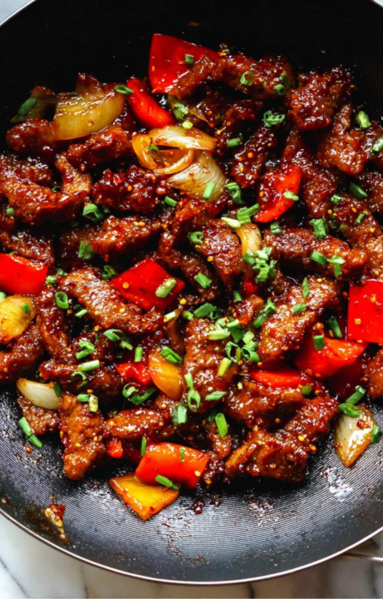 A close-up shot of the Beijing beef in the pan topped with freshly chopped green onions.