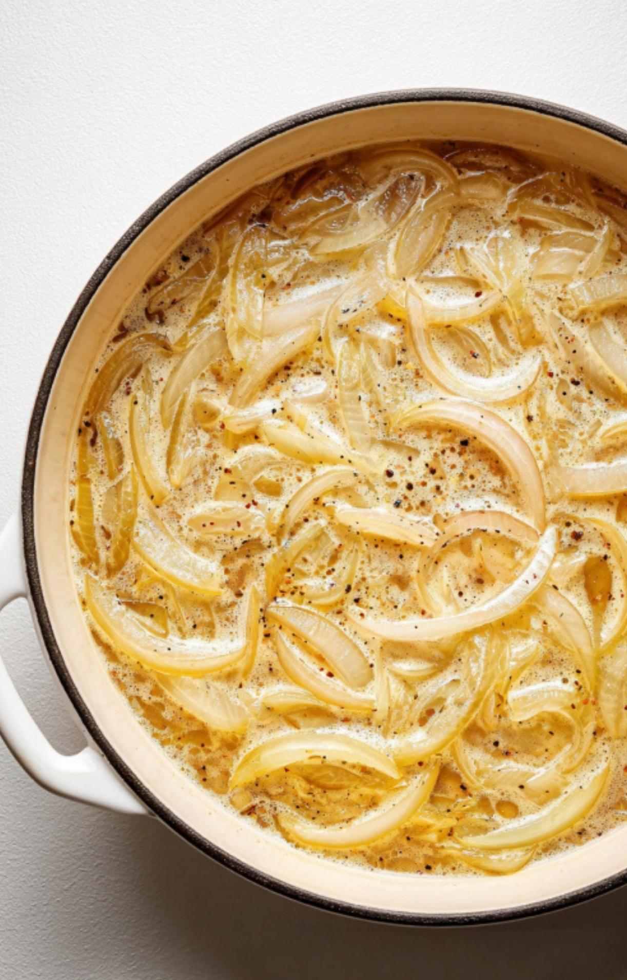 Sliced onions simmering in a seasoned beer liquid in a white pot for a beer brats on grill recipe.