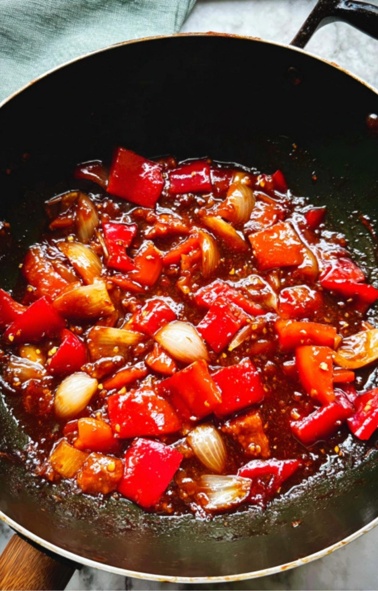 Red bell peppers and white onion chunks simmering in the savory sauce within a wok.