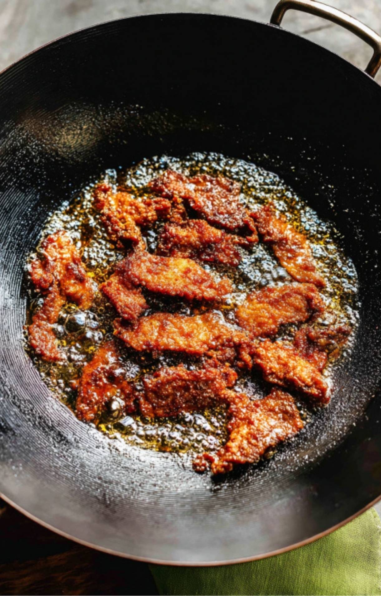 Coated beef strips deep-frying in hot oil inside a black wok until golden brown and crispy.
