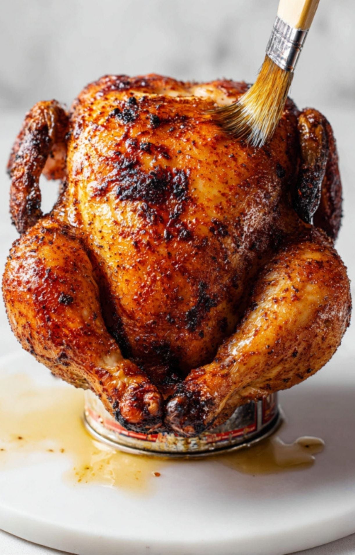 A silicone brush applying a glistening glaze or oil to the breast of a golden-brown smoked chicken.