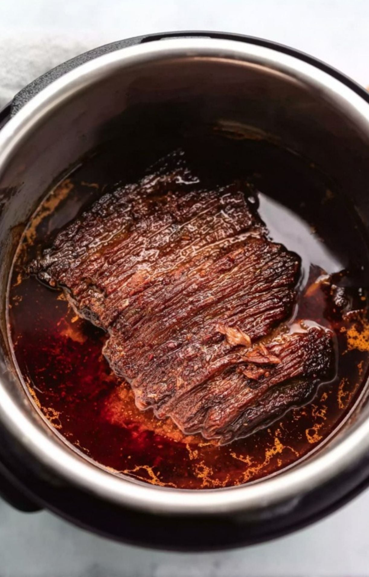A large piece of beef brisket simmering in a dark, flavorful braising liquid inside a slow cooker.